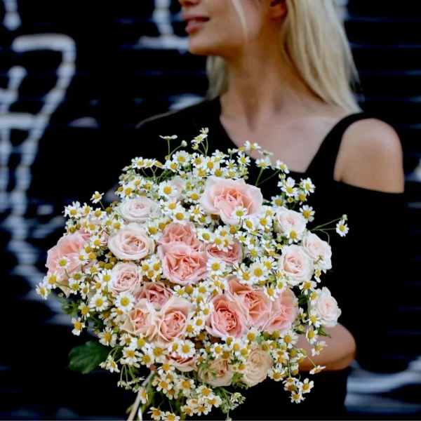 Woman holding a bouquet of pale pink roses and small white daisies