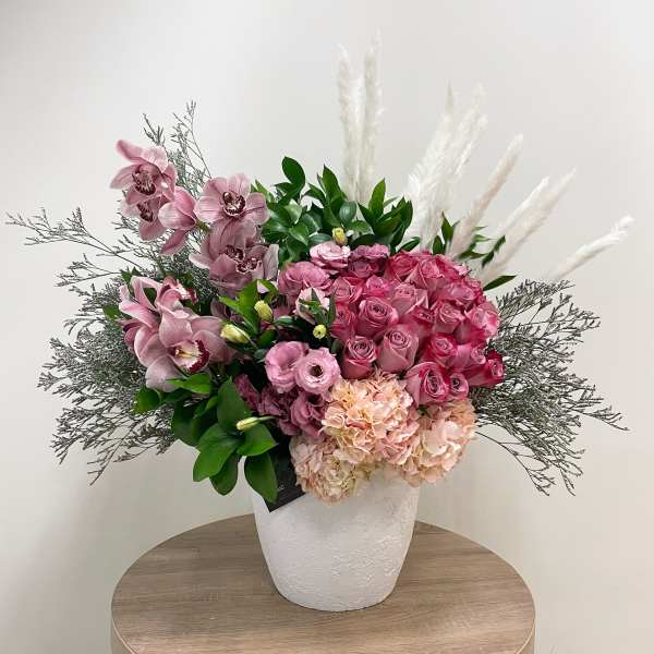 Large pink rose, orchid, hydrangea and lisianthus arrangement in a white pot with pampas plumes
