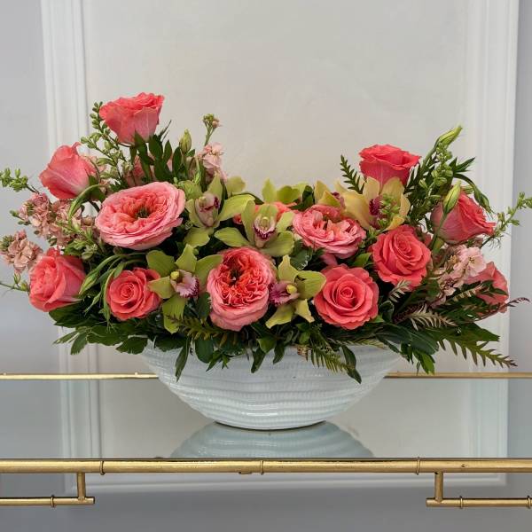 Pink roses and orchids arranged in a white bowl vase