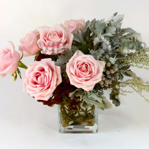 Pink roses arranged in a clear glass vase with silvery foliage