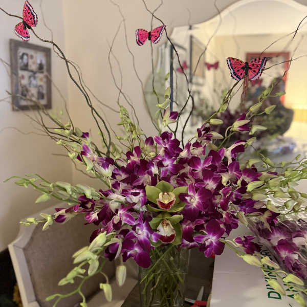 Purple orchids in a clear vase with butterfly picks