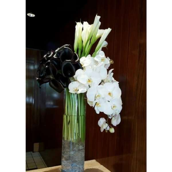 Tall white orchid and calla lily arrangement in a glass vase