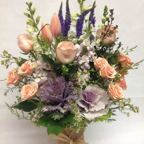 Peach roses and purple flowers arranged in a burlap-wrapped vase