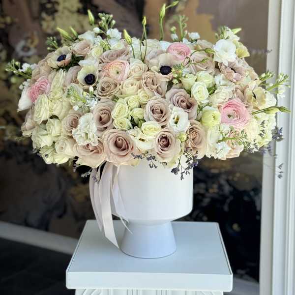Blush and white rose arrangement in a white pedestal vase