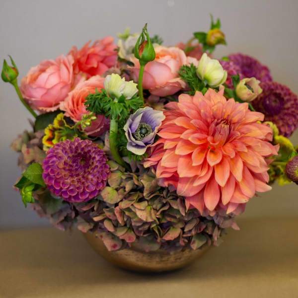 Mixed bouquet of pink, peach, and purple flowers in a low bowl vase
