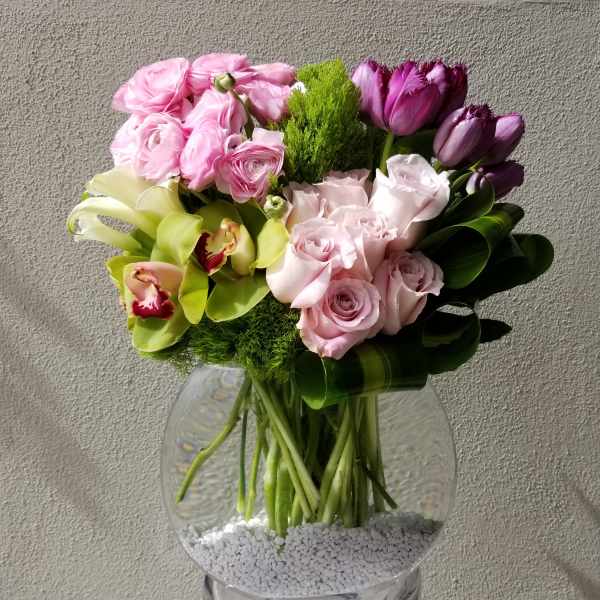 Pink and purple bouquet with roses, tulips, and orchids in a glass vase