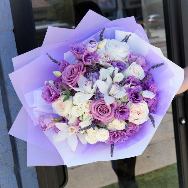 Lavender and white bouquet with roses and orchids wrapped in purple paper