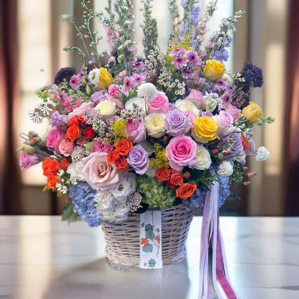 Large mixed bouquet in a wicker basket with pink, purple, yellow, and orange flowers