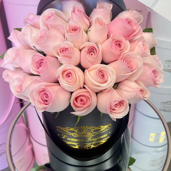 Compact arrangement of pale pink roses in a black hatbox with gold lettering