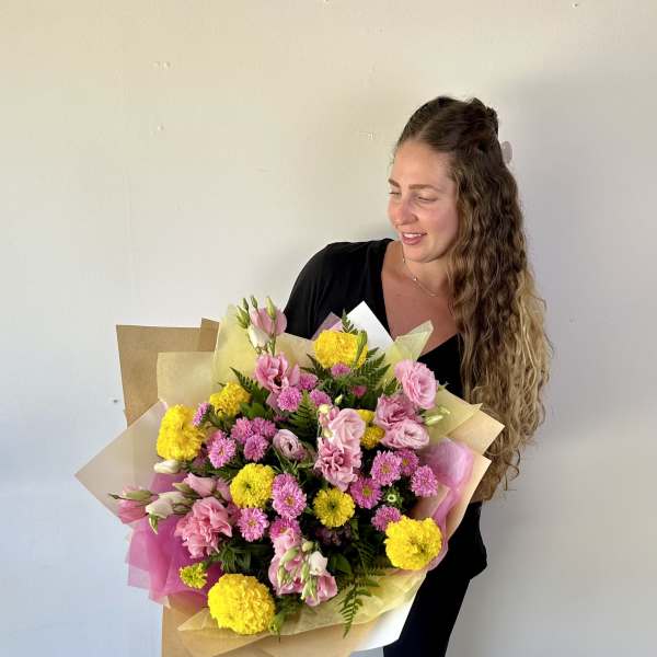 Woman holding a large bouquet of pink and yellow flowers wrapped in paper