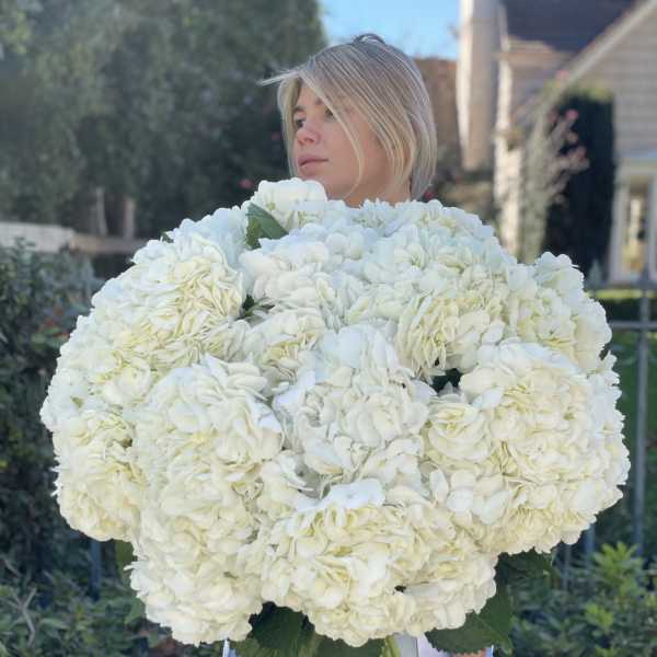 Woman holding a large bouquet of white hydrangeas in a glass vase