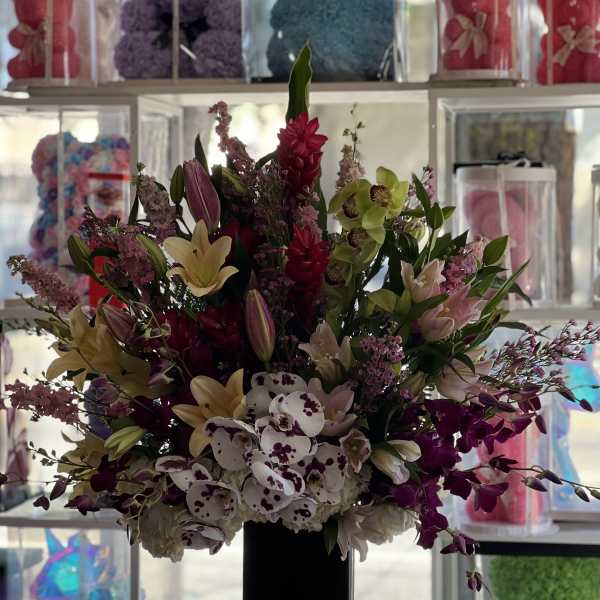 Tall mixed floral arrangement in a black vase with orchids and lilies