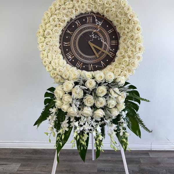 White rose funeral wreath with a clock centerpiece on a stand