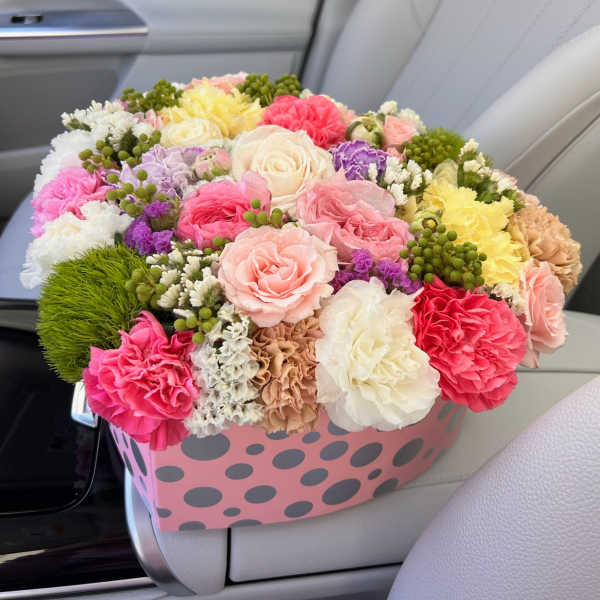 Mixed bouquet of pastel roses and carnations in a pink polka-dot box