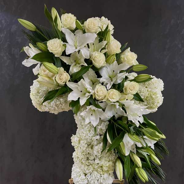 White floral cross arrangement on an easel with lilies and roses