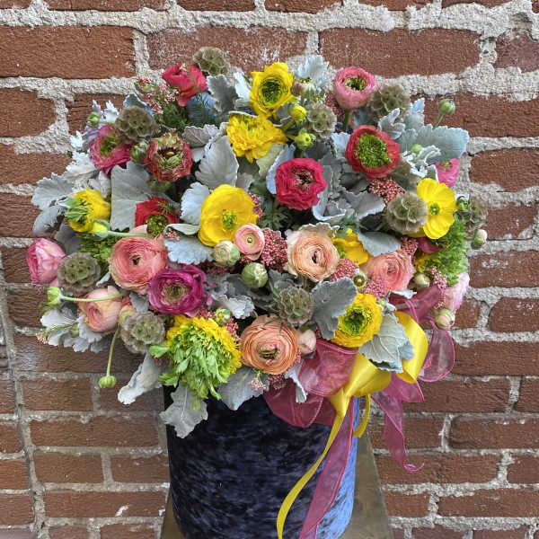 Large mixed bouquet of yellow and pink flowers in a dark velvet hatbox with trailing ribbons