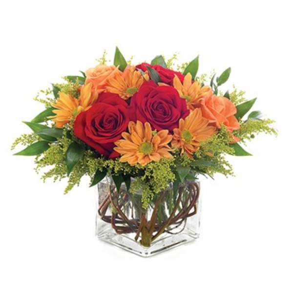 Red roses and orange daisies in a clear square vase
