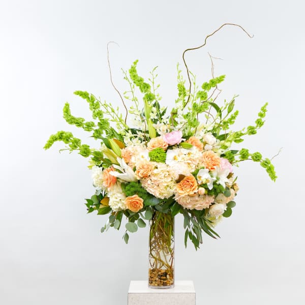 Tall floral arrangement in a clear glass vase with peach, white, and pink blooms