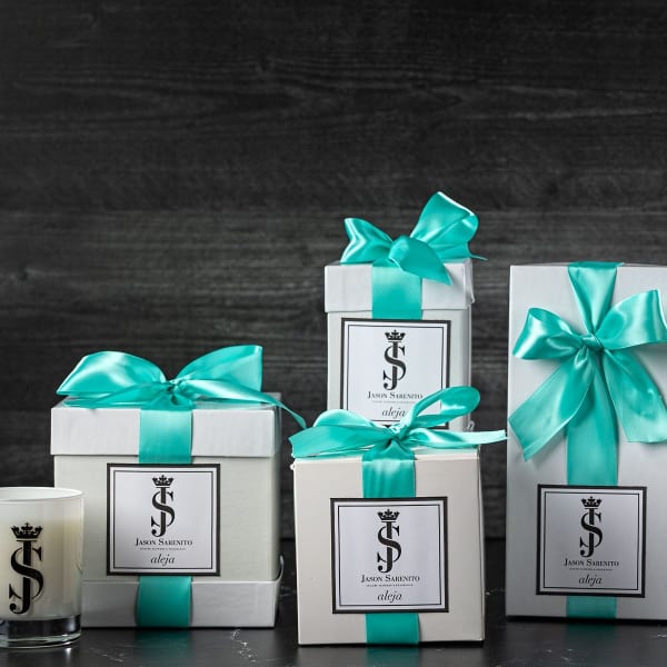 Gift boxes with teal ribbons beside a candle and a small vase of white flowers