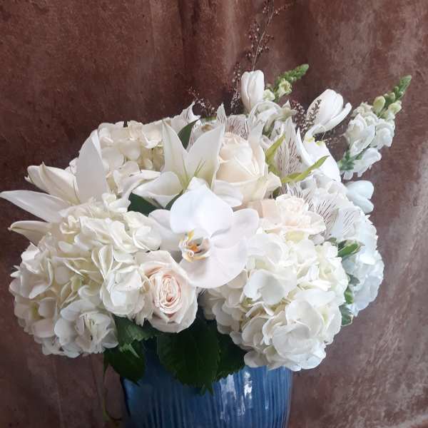 White floral arrangement in a blue vase with lilies, roses, and hydrangeas