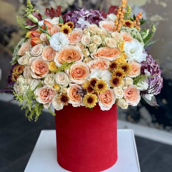 Mixed bouquet of peach, cream, and purple flowers in a red cylindrical box