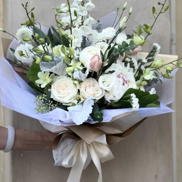 Hand-tied bouquet of white and blush flowers wrapped in lavender paper