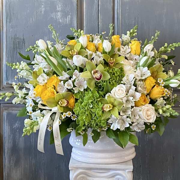 White and yellow floral arrangement in a white urn vase