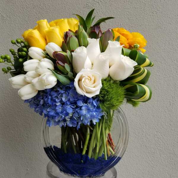 Bouquet of yellow, white, blue, and orange flowers in a clear glass vase