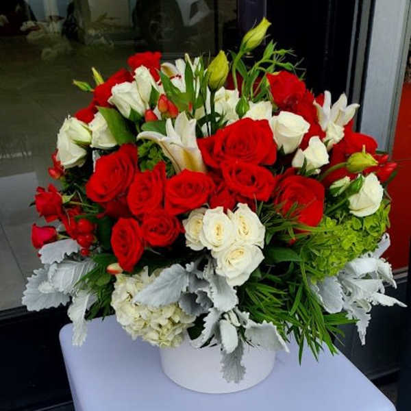 Round arrangement of red and white roses with white lilies in a white vase