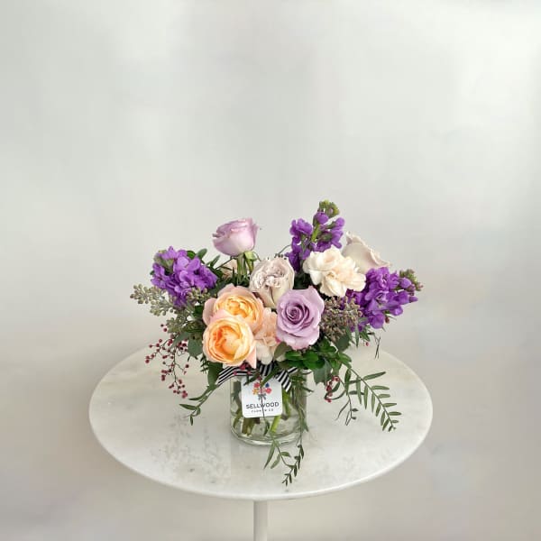 Mixed bouquet of pastel roses and purple flowers in a glass vase