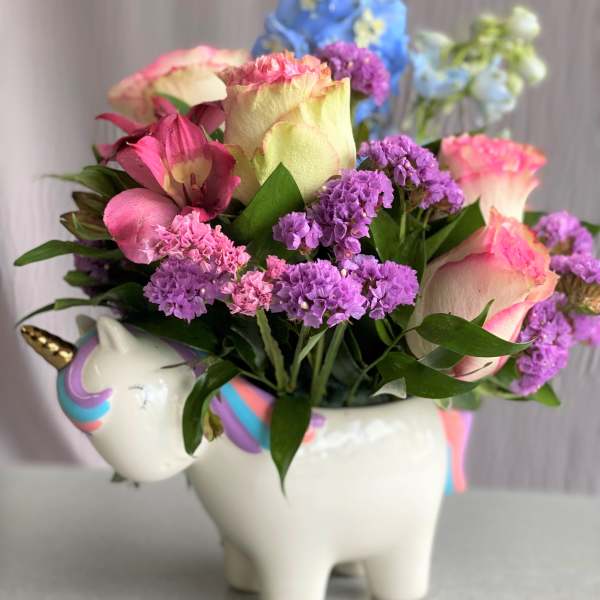 Pink and purple flowers arranged in a unicorn-shaped ceramic container