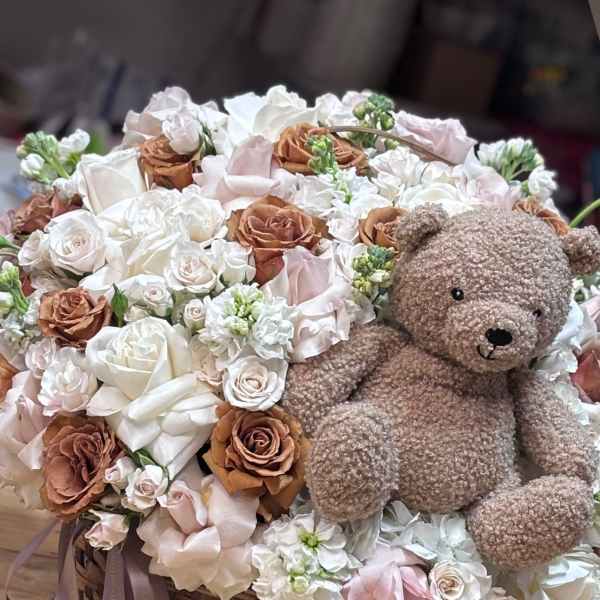 Basket arrangement of white and blush flowers with a teddy bear