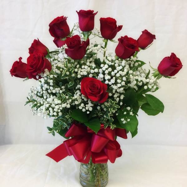 Red roses arranged in a glass vase with baby's breath and a red ribbon