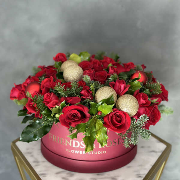 Red roses arranged in a pink round box with gold ornaments