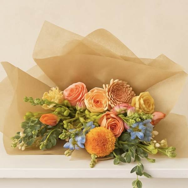 Bouquet of peach and yellow flowers wrapped in tan paper