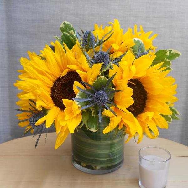 Sunflower arrangement in a green glass vase with a small candle beside it