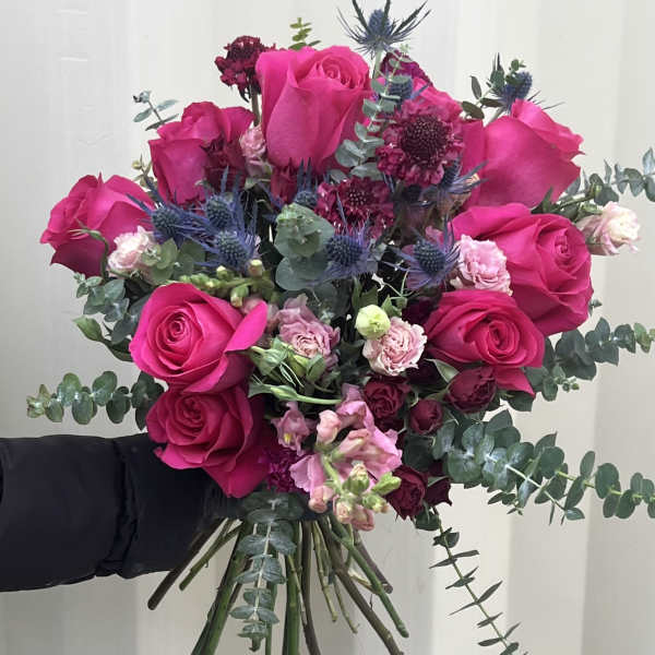Hand-tied bouquet of hot pink roses with blue thistle and eucalyptus