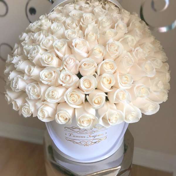 Large round hatbox filled with tightly packed ivory roses on a reflective stand