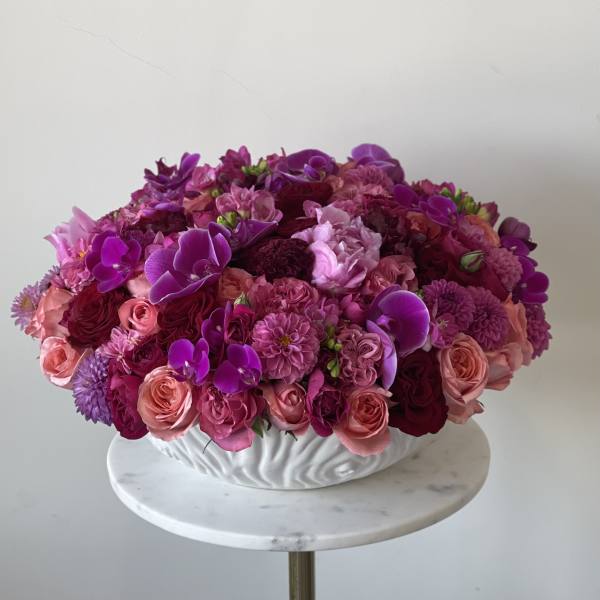 Round arrangement of pink and purple flowers in a white bowl vase