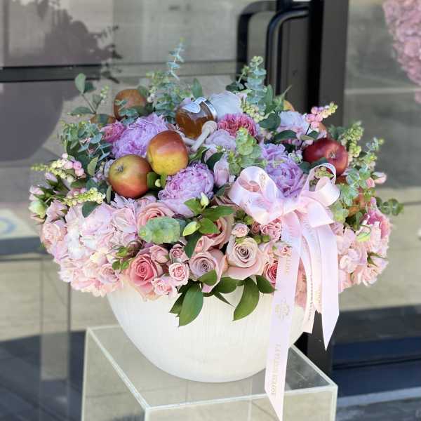 Pink floral arrangement in a white vase with apples and a ribbon bow