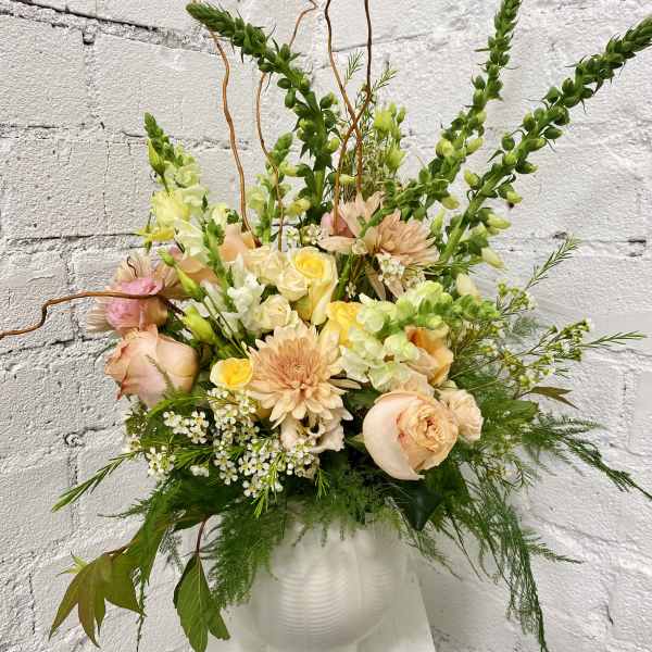Peach and yellow floral arrangement in a white vase with tall green spikes