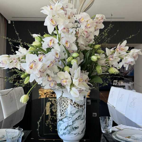 Large white orchid arrangement in a decorative vase on a dining table