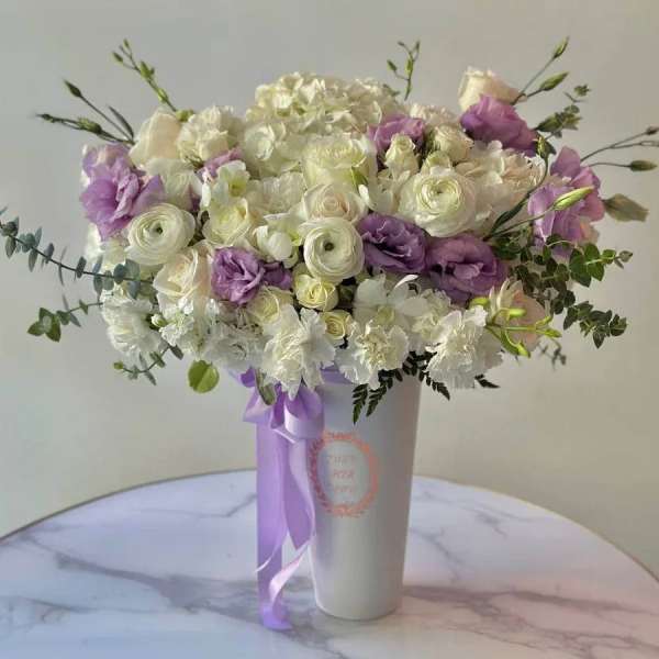 White and lavender bouquet in a tall white vase with a purple ribbon