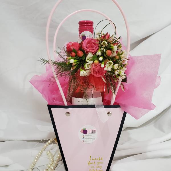 Pink rose arrangement in a gift bag with a bottle and pearl strands