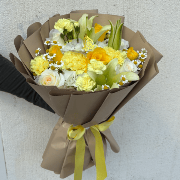 Hand-tied bouquet of yellow and white flowers wrapped in tan paper with a yellow ribbon