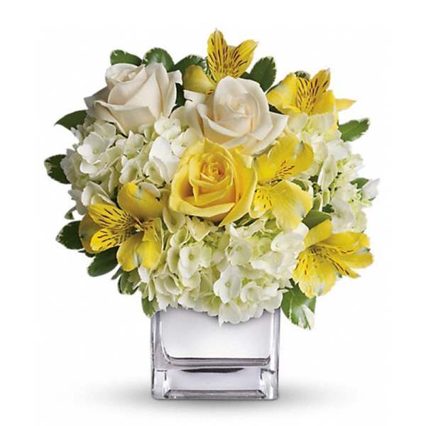 Yellow and white flower arrangement in a clear square vase