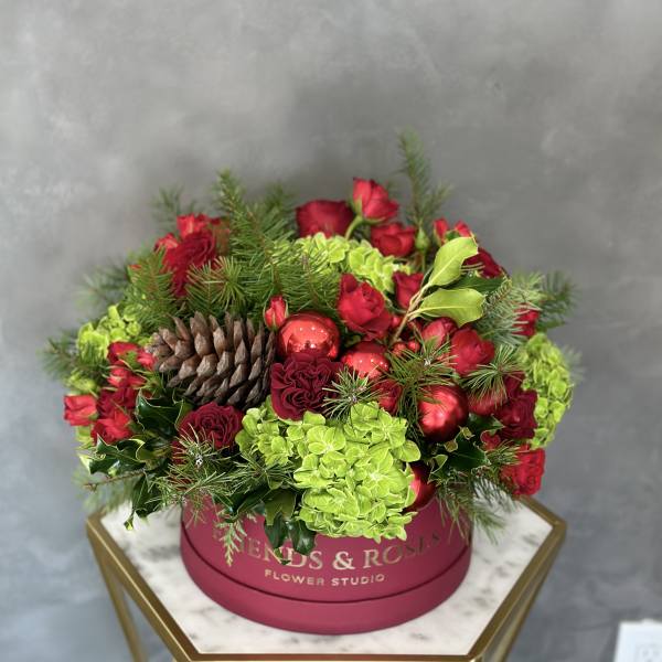 Red roses and green hydrangeas in a pink round box with pinecones and ornaments