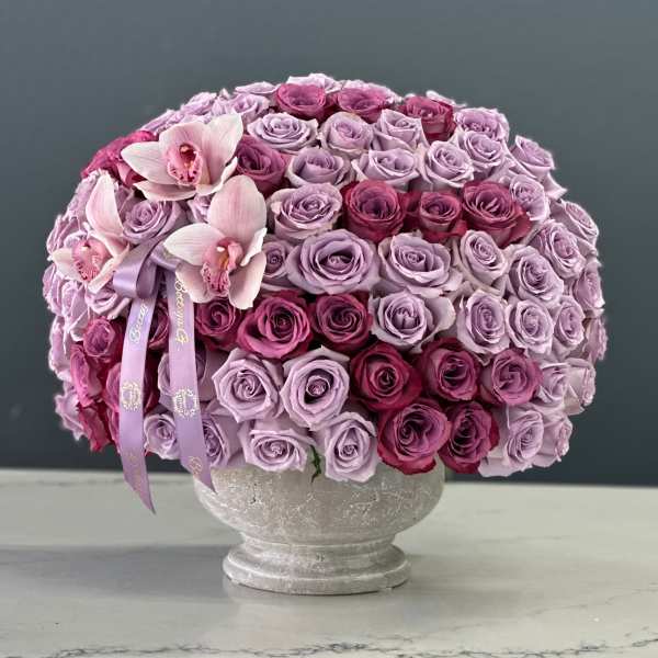 Lavender and pink rose arrangement in a gray pedestal vase with orchids