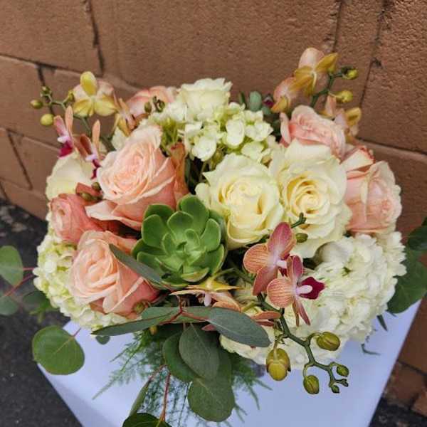 Low arrangement of peach and cream roses, white hydrangea, orchids and a green succulent in a compact design