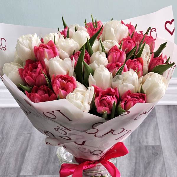 Bouquet of pink and white tulips in a glass vase with a red ribbon